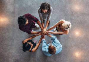 Young people putting their hands on top of each other symbolizing unity and teamwork. Diverse group of students stacking their hands.